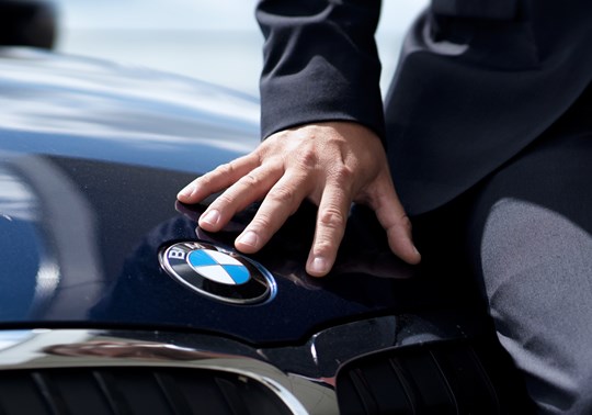 BMW-ejers hånd ved BMW logoet på kølerhjelmen af bilen 